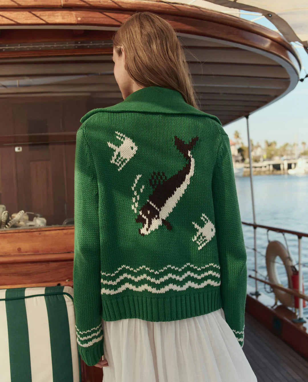Person wearing a green sweater with whale design on a boat