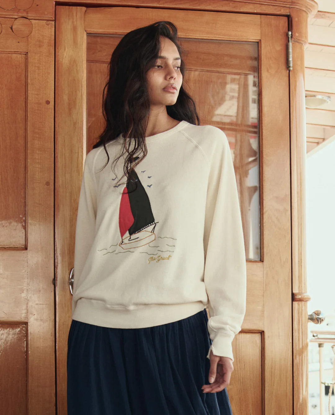 Woman wearing a white sweater with a graphic design, standing in front of a wooden door.