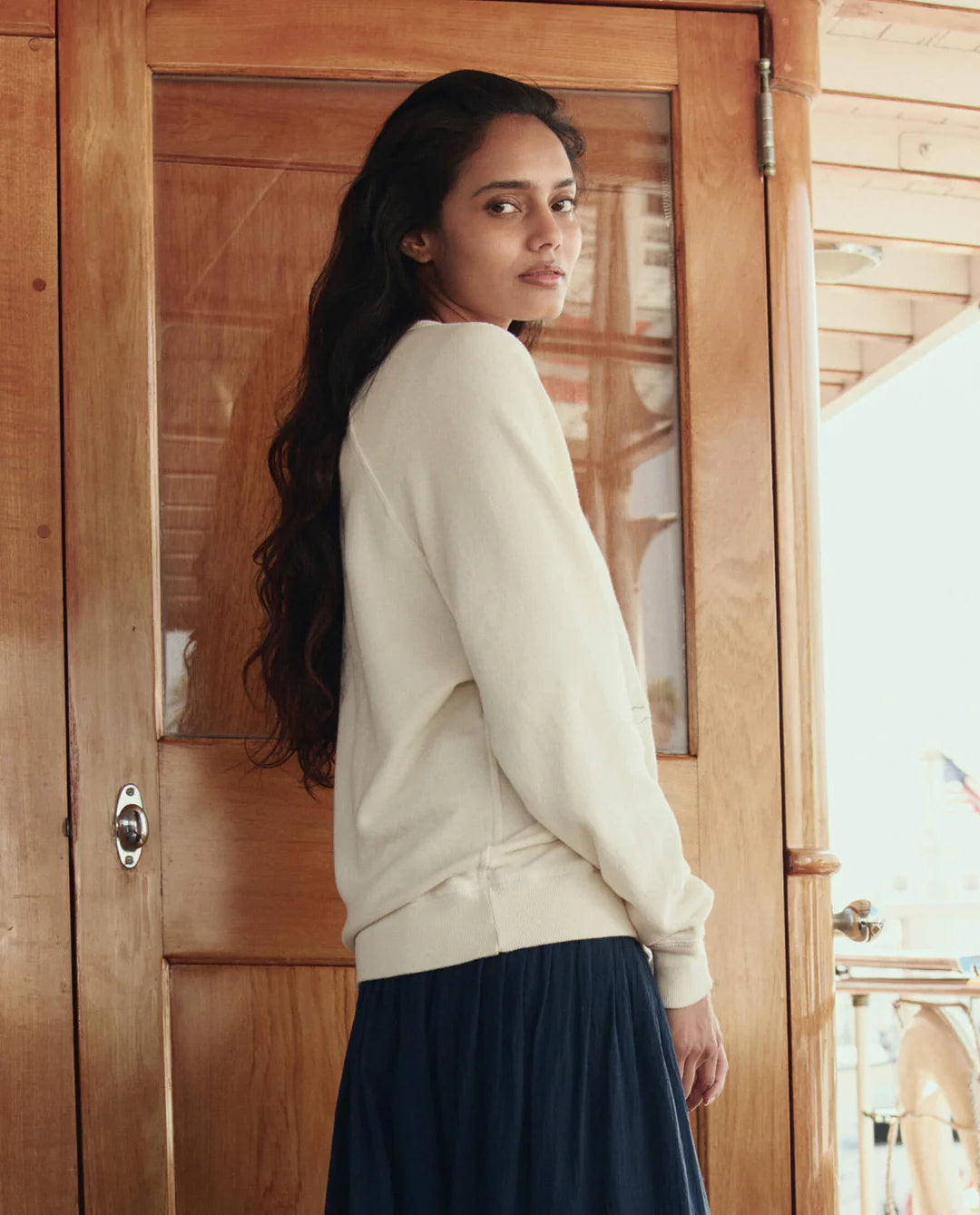 Woman wearing a white sweater and dark skirt standing in front of a wooden door.