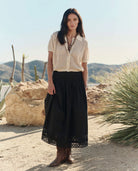 Woman in a white blouse and black skirt standing in a desert landscape with mountains in the background.