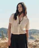 Woman wearing a beige knitted cardigan over a black top with a desert landscape in the background