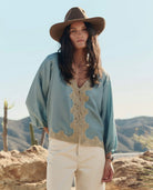 Woman wearing a light blue blouse with lace details and a wide-brimmed hat in a desert setting.
