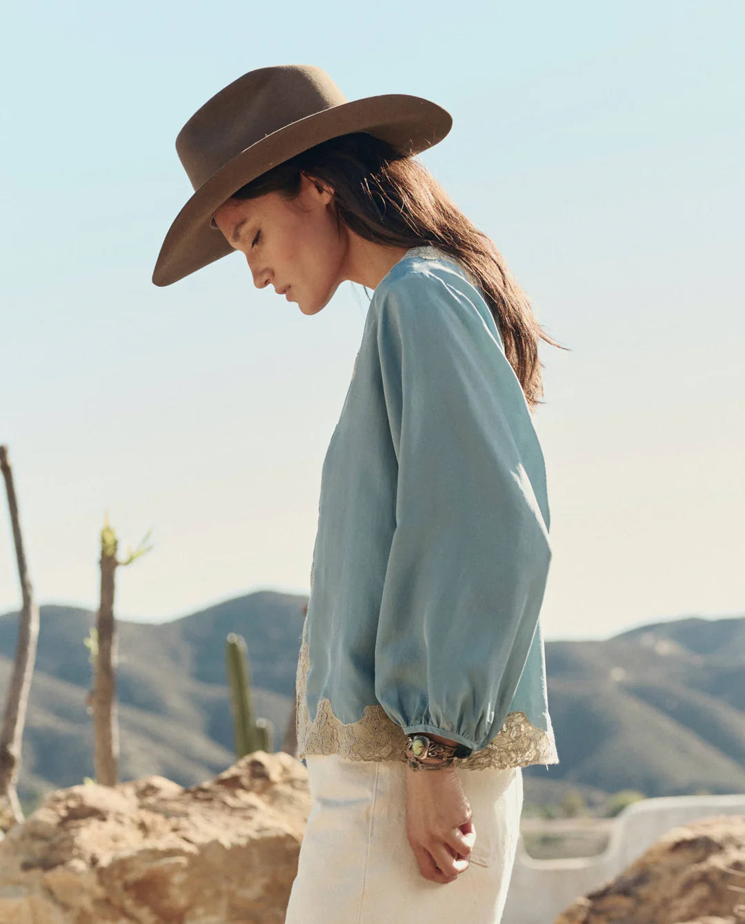 Woman wearing a brown hat and light blue blouse with lace trim in a desert setting