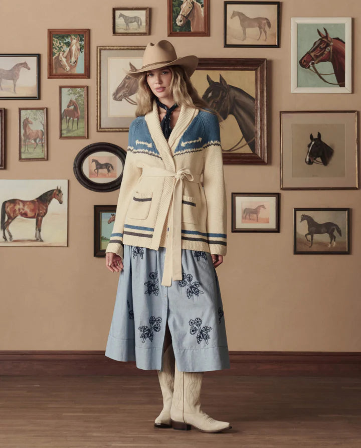 Woman in a stylish outfit with a cowboy hat standing in a room with horse-themed decor.