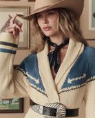 Woman wearing a patterned cardigan and cowboy hat indoors