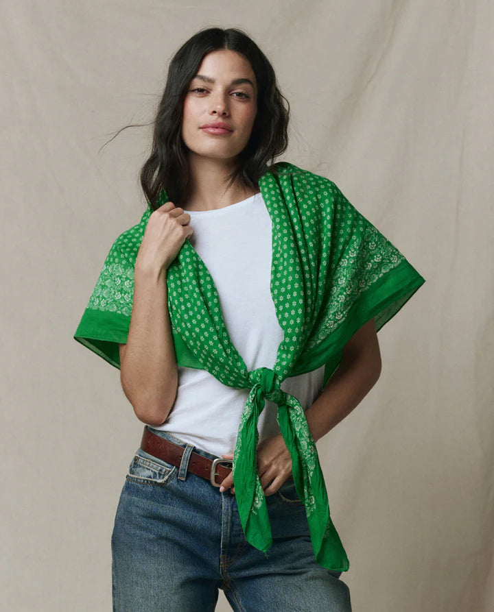 Woman wearing a green patterned scarf over a white shirt and jeans on a beige background