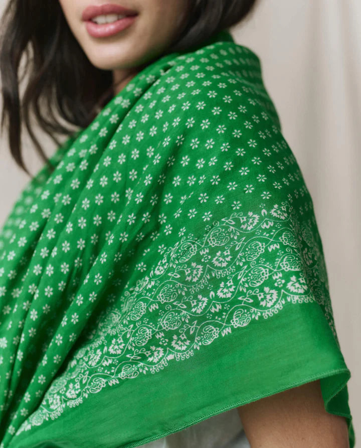 Green fabric with white floral patterns draped over a person, with a neutral background.