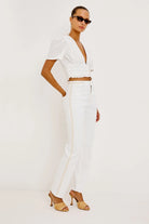Woman wearing a white outfit with sunglasses on a plain background