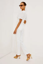 Woman wearing a white outfit with gold heels on a white background