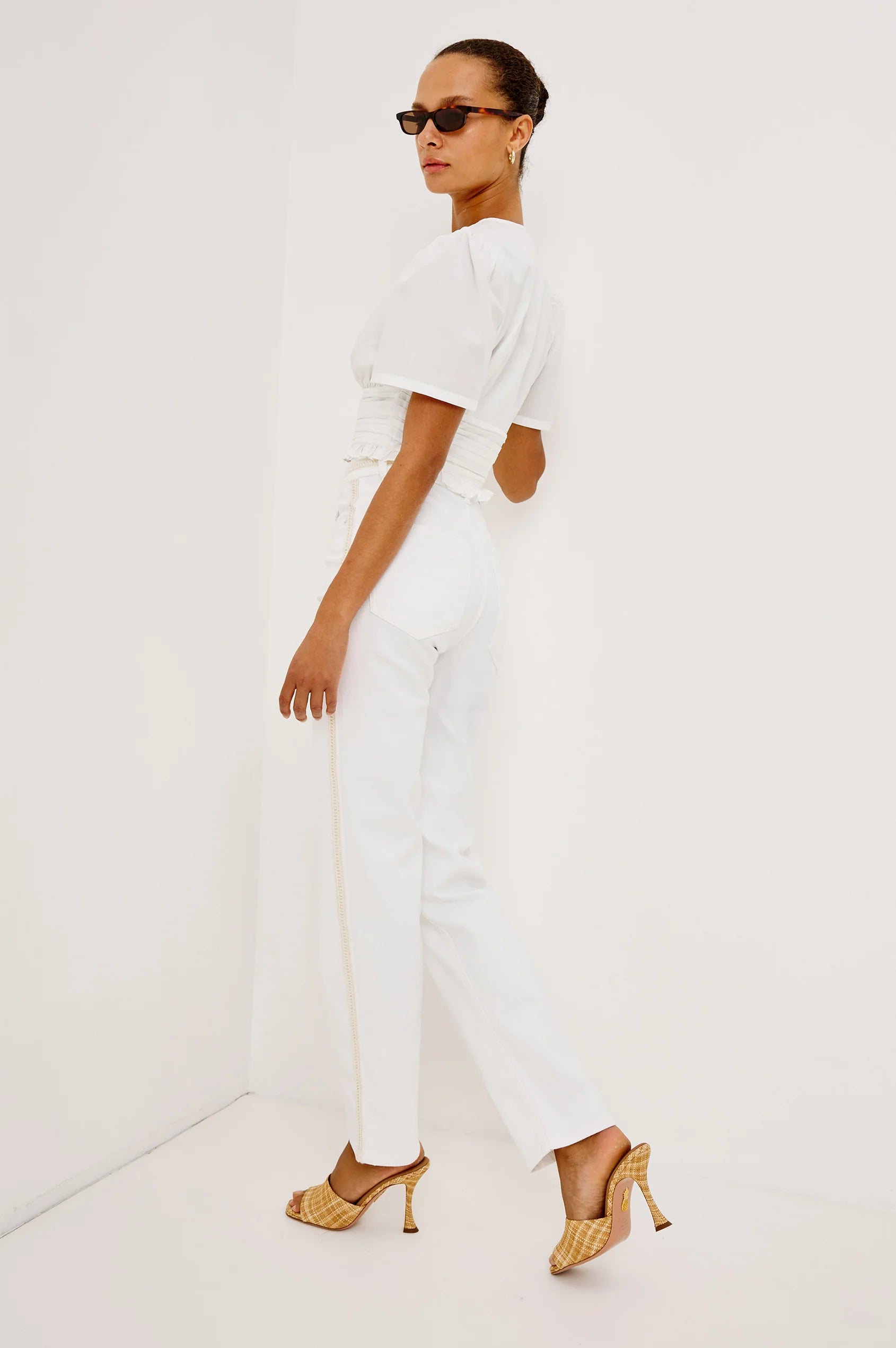 Woman wearing a white outfit with gold heels on a white background