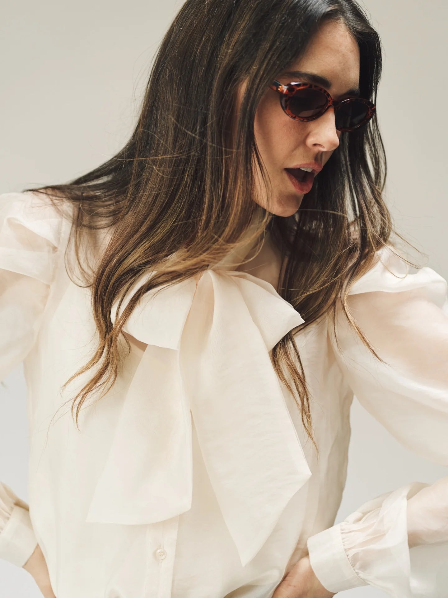 Woman wearing a light-colored blouse with sheer sleeves against a neutral background