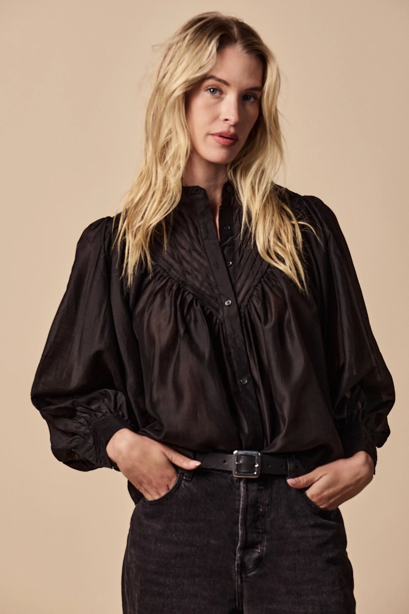 Woman wearing a black blouse with puffed sleeves against a beige background