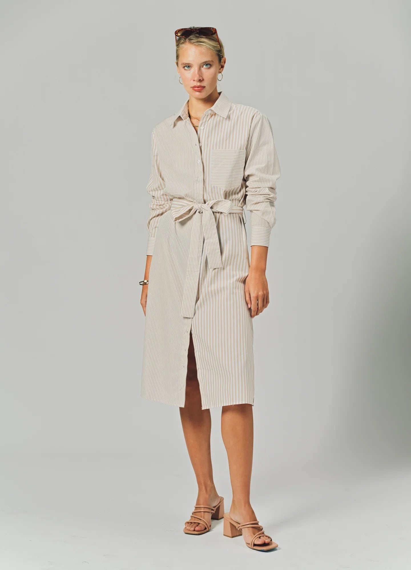 Woman wearing a beige dress with a belt on a gray background