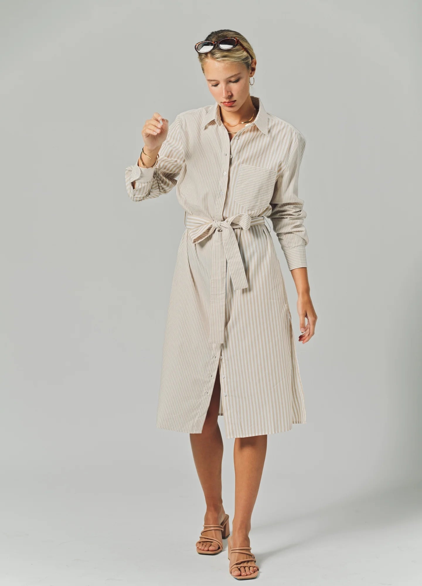 Woman wearing a beige striped shirt dress on a plain background