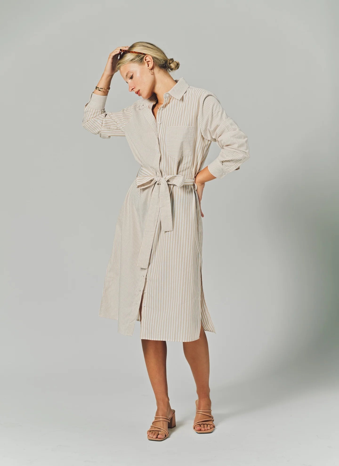 Woman wearing a beige ribbed dress with a belt on a plain background