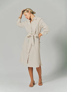 Woman wearing a beige ribbed dress with a belt on a plain background