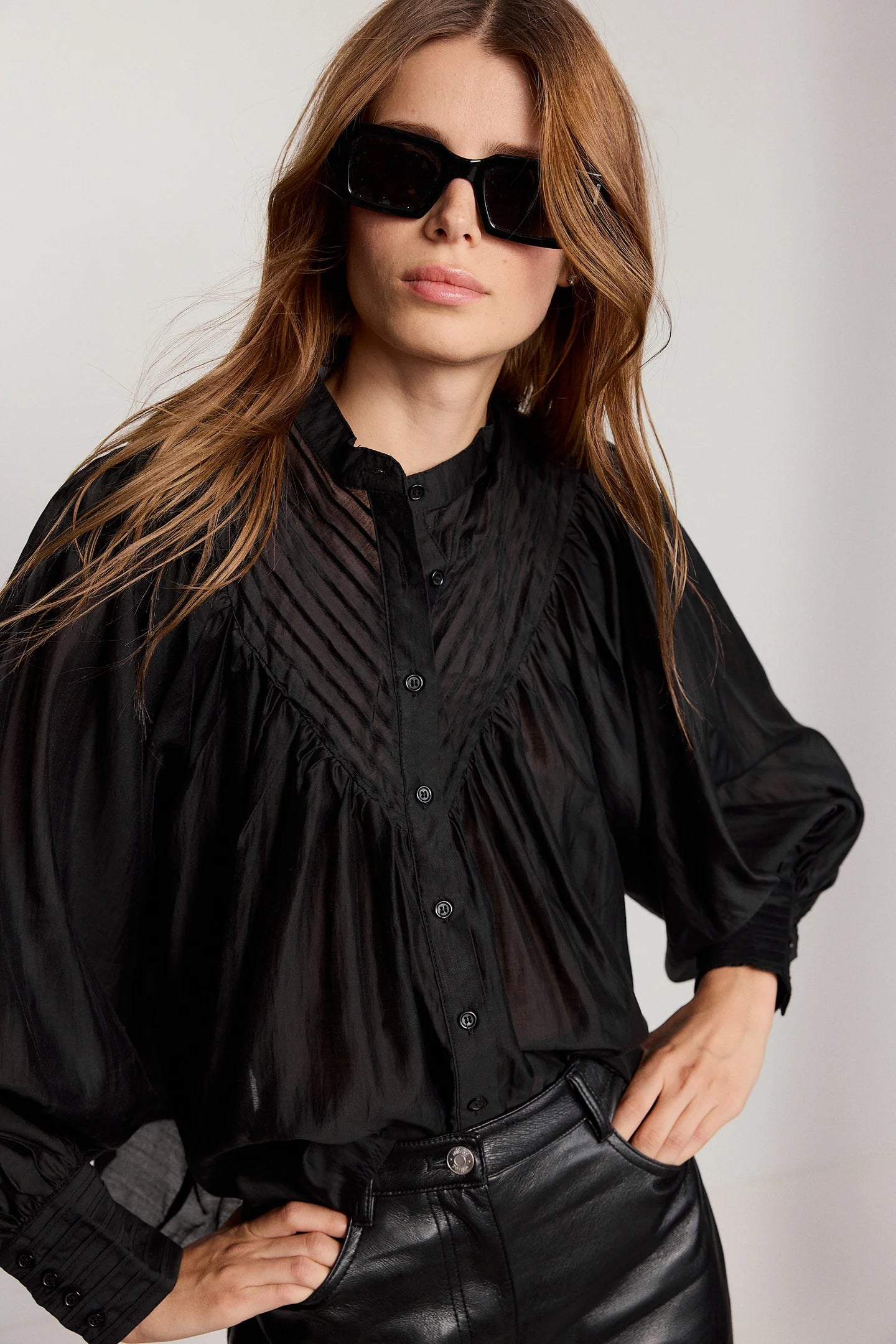Woman wearing a black blouse and sunglasses against a plain background