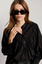 Woman wearing a black blouse and sunglasses against a plain background
