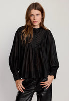 Woman wearing a black blouse and black pants against a plain background