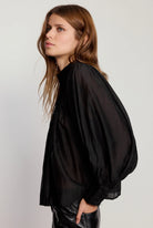 Woman wearing a black blouse with balloon sleeves against a white background