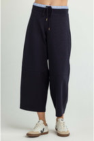 A person wearing dark navy wide-leg cropped sweatpants with a drawstring waist and light blue striped elastic band, paired with white sneakers, against a light gray studio background.