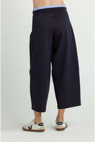 A model is shown from the back wearing dark navy wide-leg cropped pants with a light blue and white striped waistband, paired with beige and navy sneakers, against a plain light gray studio background.