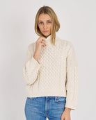 Woman wearing a cream knitted sweater and blue jeans on a white background
