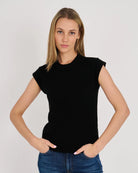 A woman modeling a black short-sleeve crewneck top with cap sleeves, paired with blue jeans, against a plain light gray studio background.