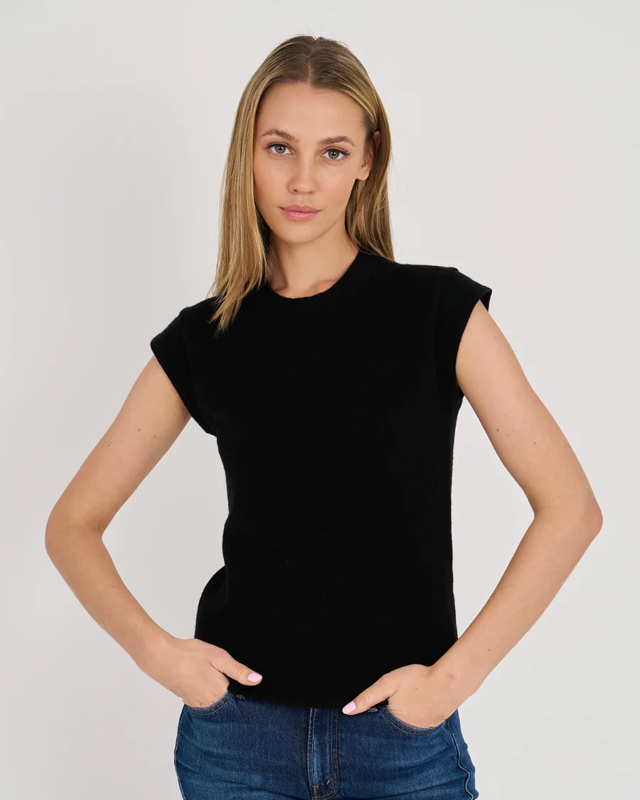 A woman modeling a black short-sleeve crewneck top with cap sleeves, paired with blue jeans, against a plain light gray studio background.