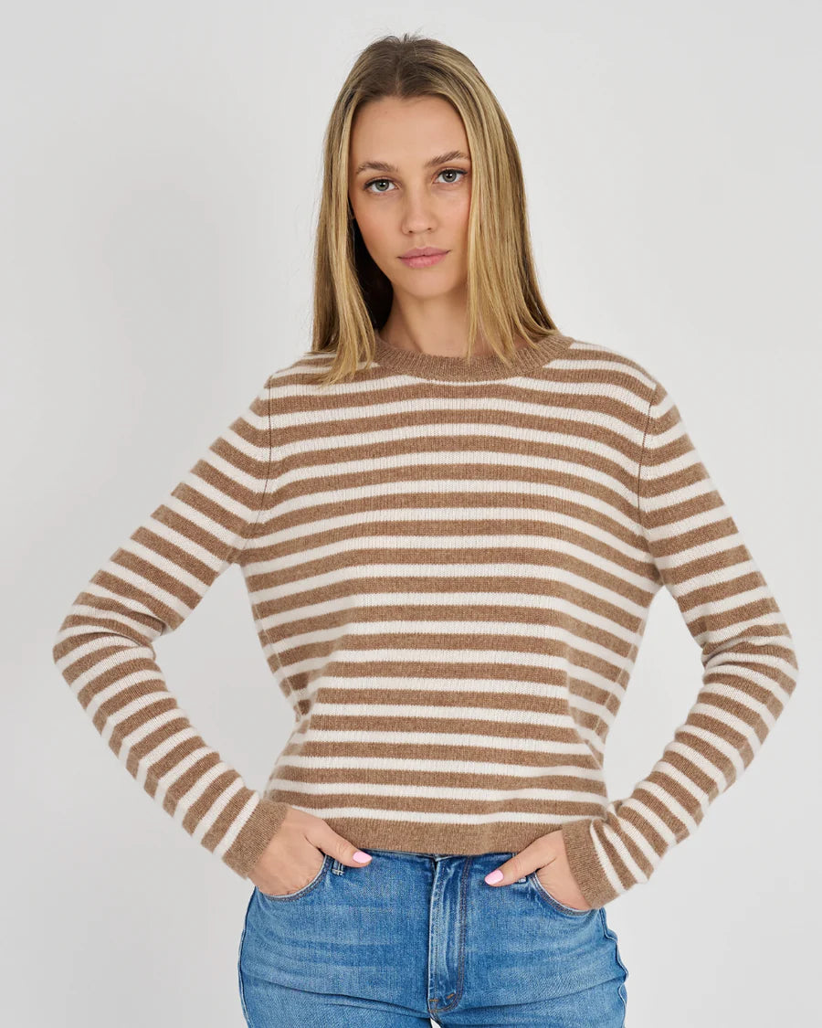 A woman modeling a cropped, long-sleeve knit sweater with horizontal brown and beige stripes, paired with blue jeans, against a light gray studio background.