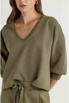 A woman wearing an olive green knit top with a V-neckline and elbow-length sleeves, paired with matching olive green bottoms against a plain light background.