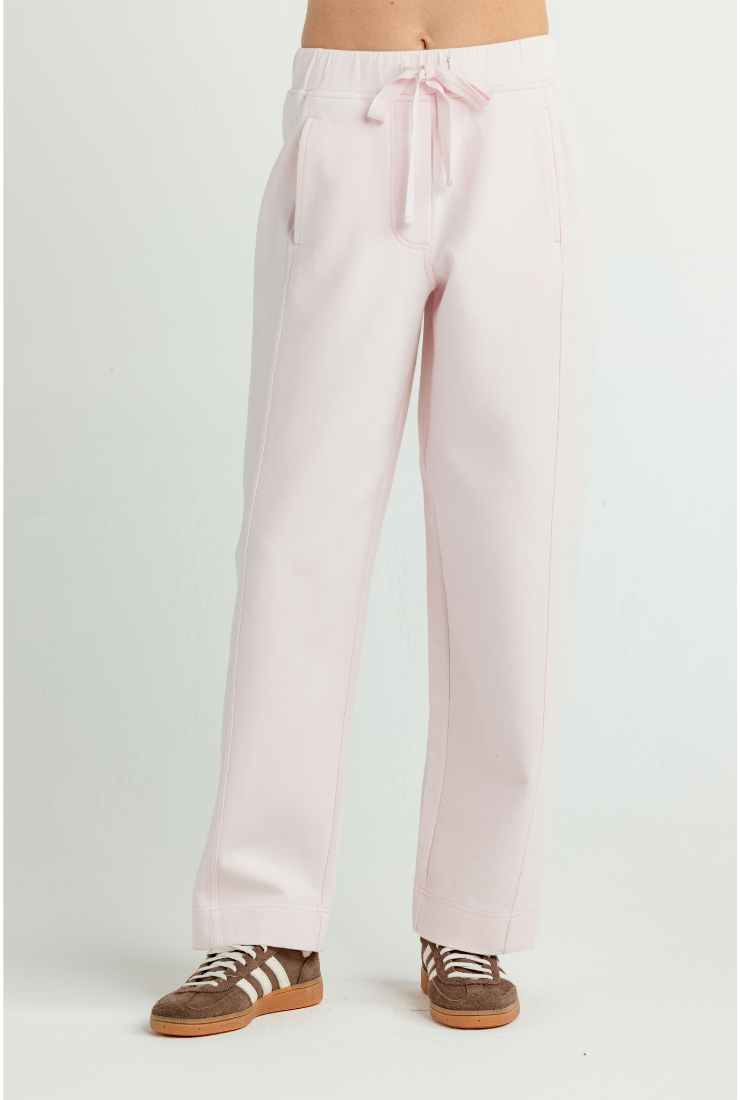 A person wearing light pink wide-leg drawstring pants and brown sneakers, shown from the waist down against a plain light gray studio background.