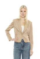 A blonde woman modeling a beige corduroy blazer over a white top and blue jeans, standing against a plain white background.