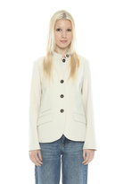 A blonde woman modeling a cream-colored, high-neck button-front blazer with dark buttons, paired with blue jeans, against a plain white background.