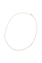 A delicate gold chain necklace with small, evenly spaced clear round beads, displayed in a circular shape against a plain white background.