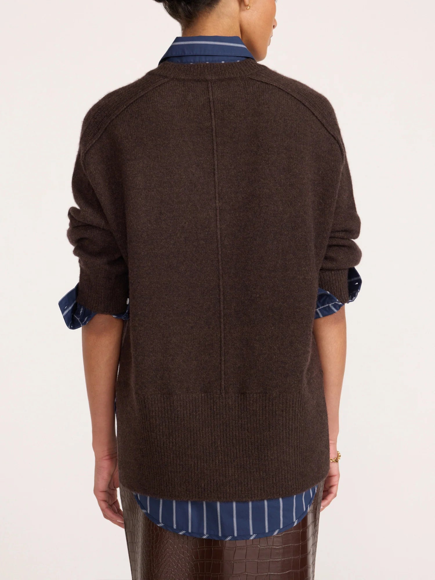 A person shown from the back wearing a dark brown knit sweater over a blue and white striped button-down shirt, against a plain light background.