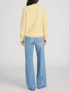 Person wearing a yellow sweater and blue jeans on a plain background