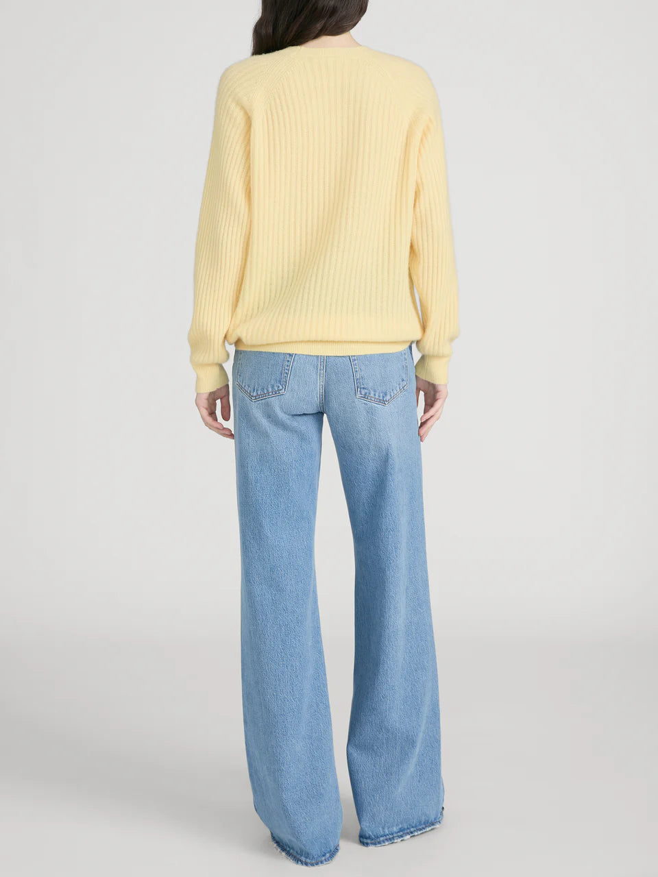 Person wearing a yellow sweater and blue jeans on a plain background