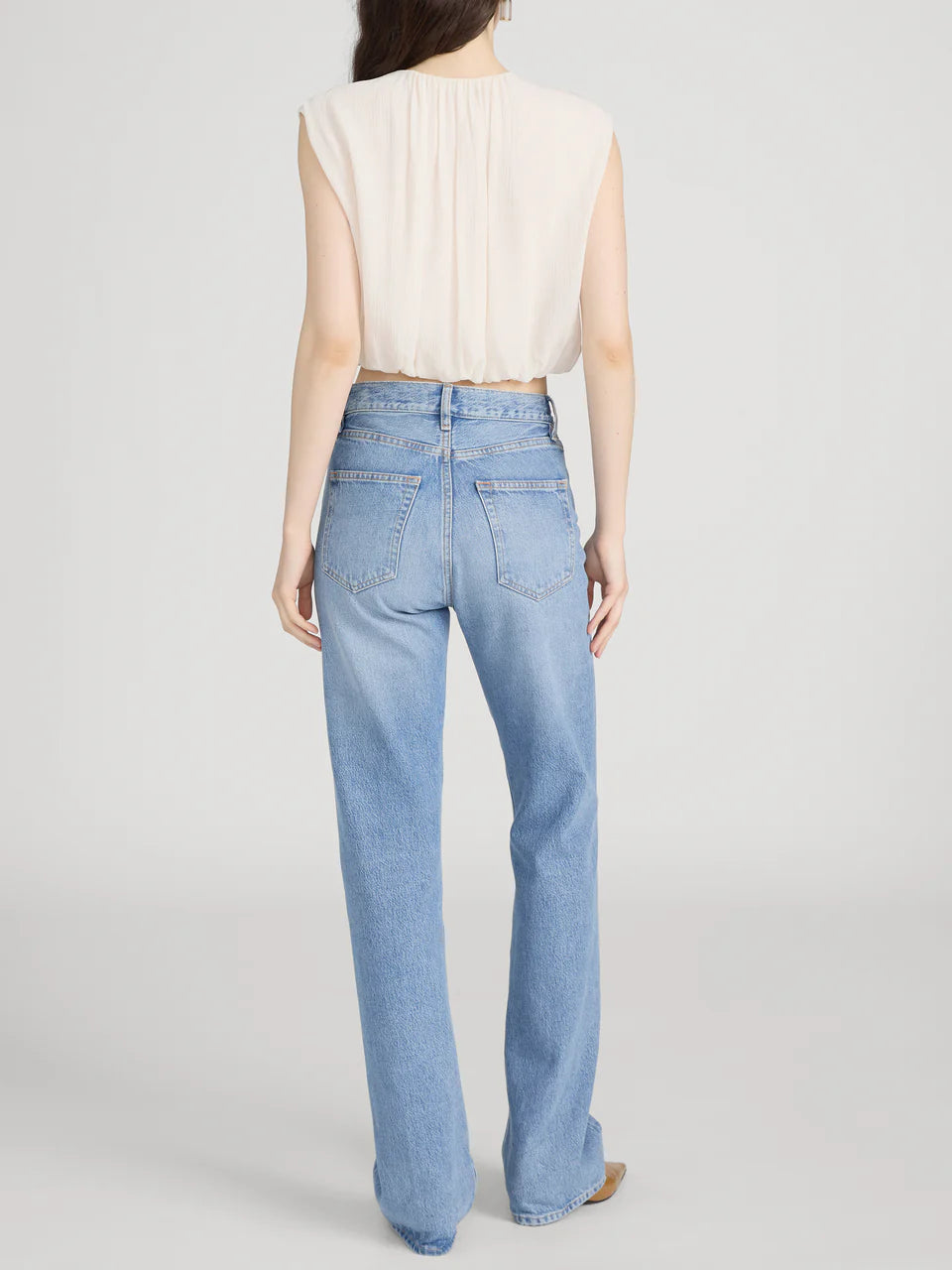 Person wearing light blue jeans and a beige top on a plain background