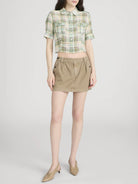 Person wearing a plaid shirt and beige skirt on a white background