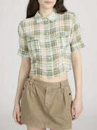 Person wearing a green plaid shirt and beige skirt on a white background