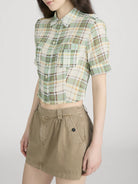 Person wearing a green plaid shirt and beige skirt on a white background