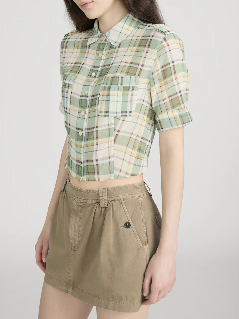 Person wearing a green plaid shirt and beige skirt on a white background