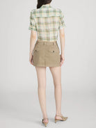 Person wearing a green plaid shirt and beige skirt on a white background