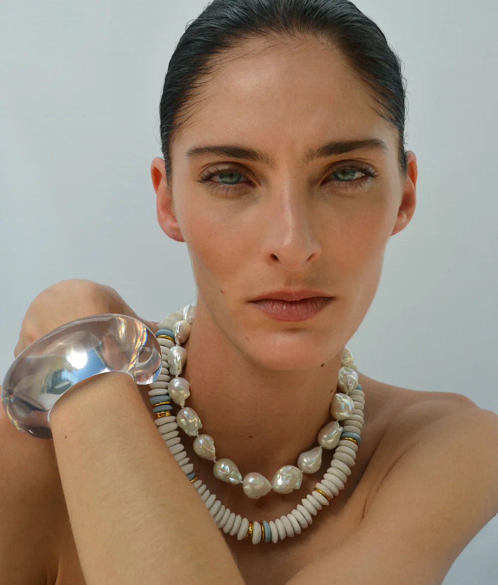 Woman wearing a silver bracelet and pearl necklace against a plain background