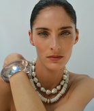 Woman wearing a silver bracelet and pearl necklace against a plain background