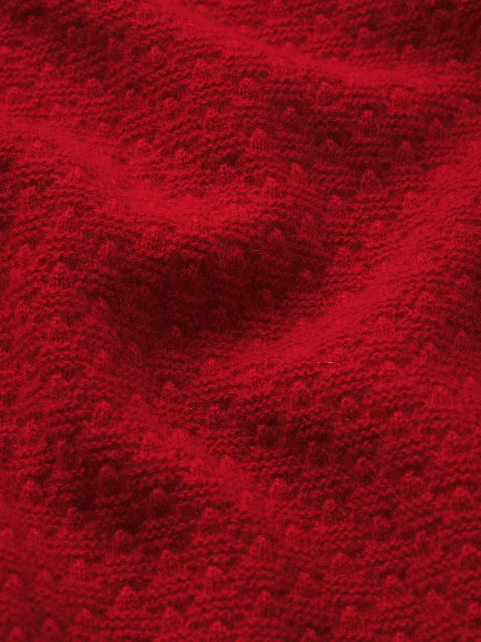 A close-up of a textured red knit fabric with a raised bumpy or terry-like surface, filling the entire frame.