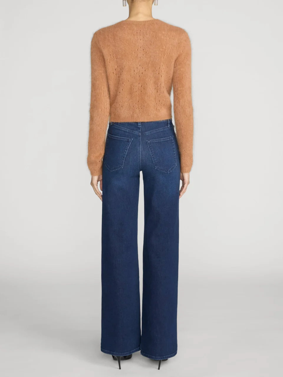 A model shown from the back wearing a fuzzy cropped tan sweater and dark blue wide-leg jeans against a light gray studio background.