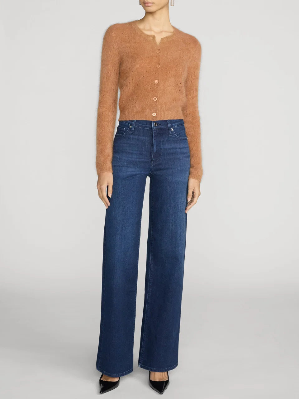 A model wearing a cropped, fuzzy tan cardigan and high-waisted, wide-leg blue jeans against a light gray studio background.