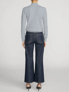 A model shown from the back wearing a light gray ribbed mock-neck sweater and dark blue wide-leg denim jeans, paired with black high heels, against a light gray studio background.